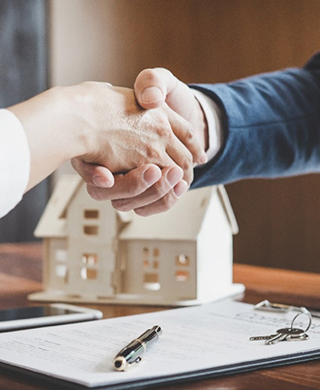 Handshake over real estate contract and house model, symbolizing home insurance deals.