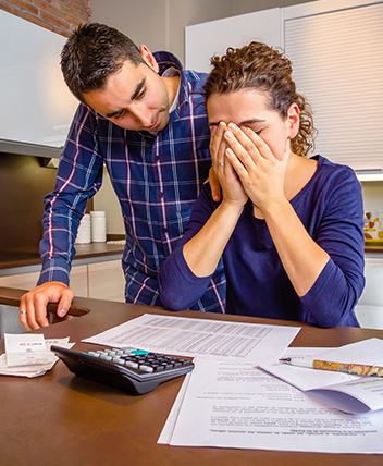 Couple stressed while reviewing bills, illustrating financial struggle and debt relief.