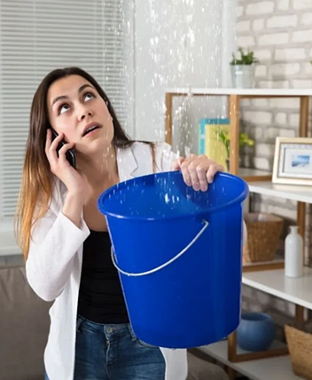 Woman holding bucket under leaking ceiling while on the phone.